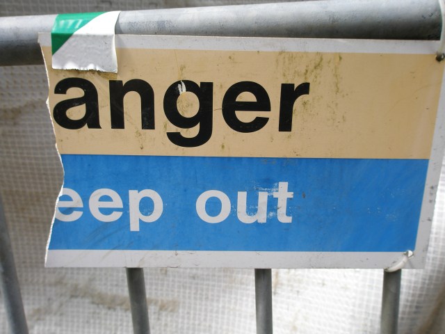 A metal barrier where the sign is broken, so that the original 'Danger, keep out' reads 'anger, eep out.'