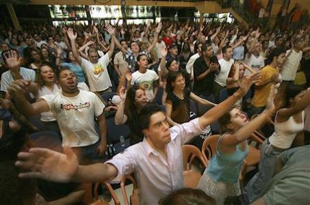 A congregation praising God, many of whom are raising thair hands to God.
