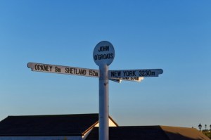Signpost at John O'Groats, Scotland against a clear blue sky.