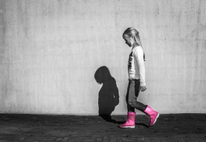 A girl wearing pink wellington boots is walking away, looking sad.
