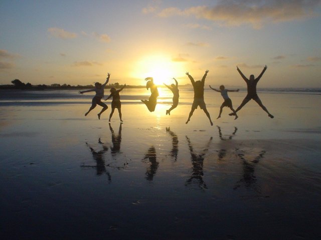 Seven people jumping for joy, silhouetted against a sunset.