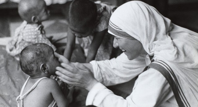 A smiling nun, Mother Theresa of Calcutta, looks on a small chi