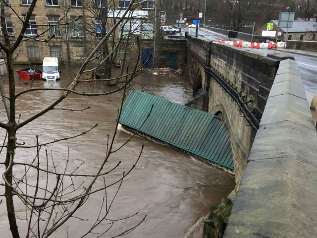 Shipping container on floodwater, stuck under the arches of Elland Bridge.