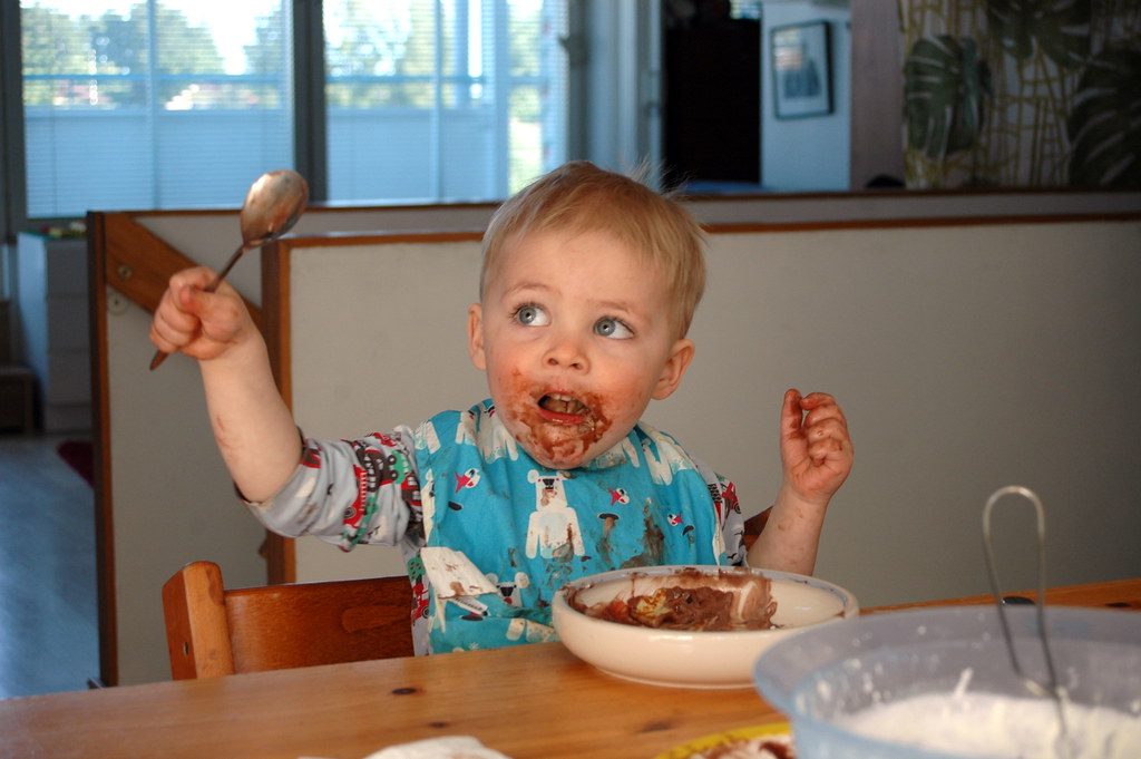 A young child eating chocolate ice cream, with mess all over their face and bib.