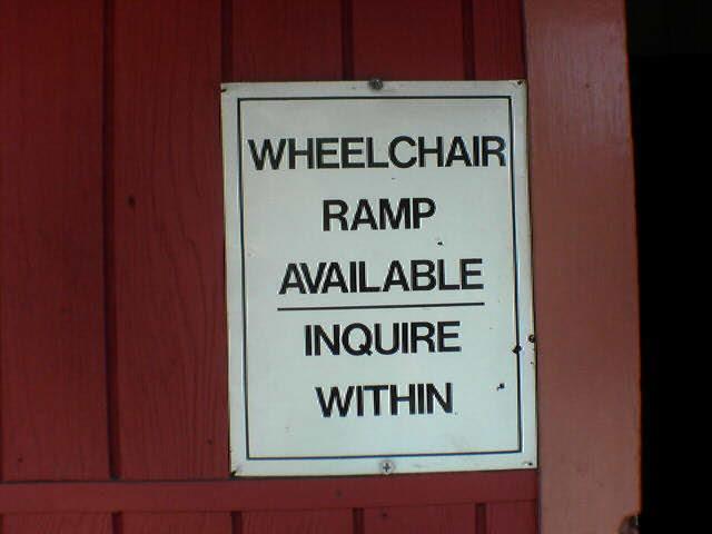 A sign on a varnished wood door saying, "Wheelchair ramp available, inquire within".