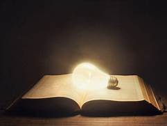 An unconnected lightbulb is illuminated and sitting on an open Bible/