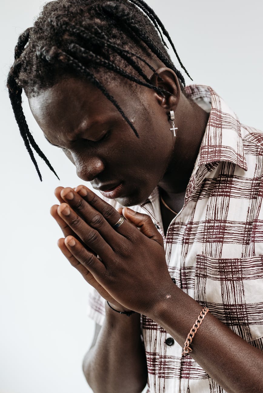 A black man with a cross earring has hands held together and head bowed in prayer.