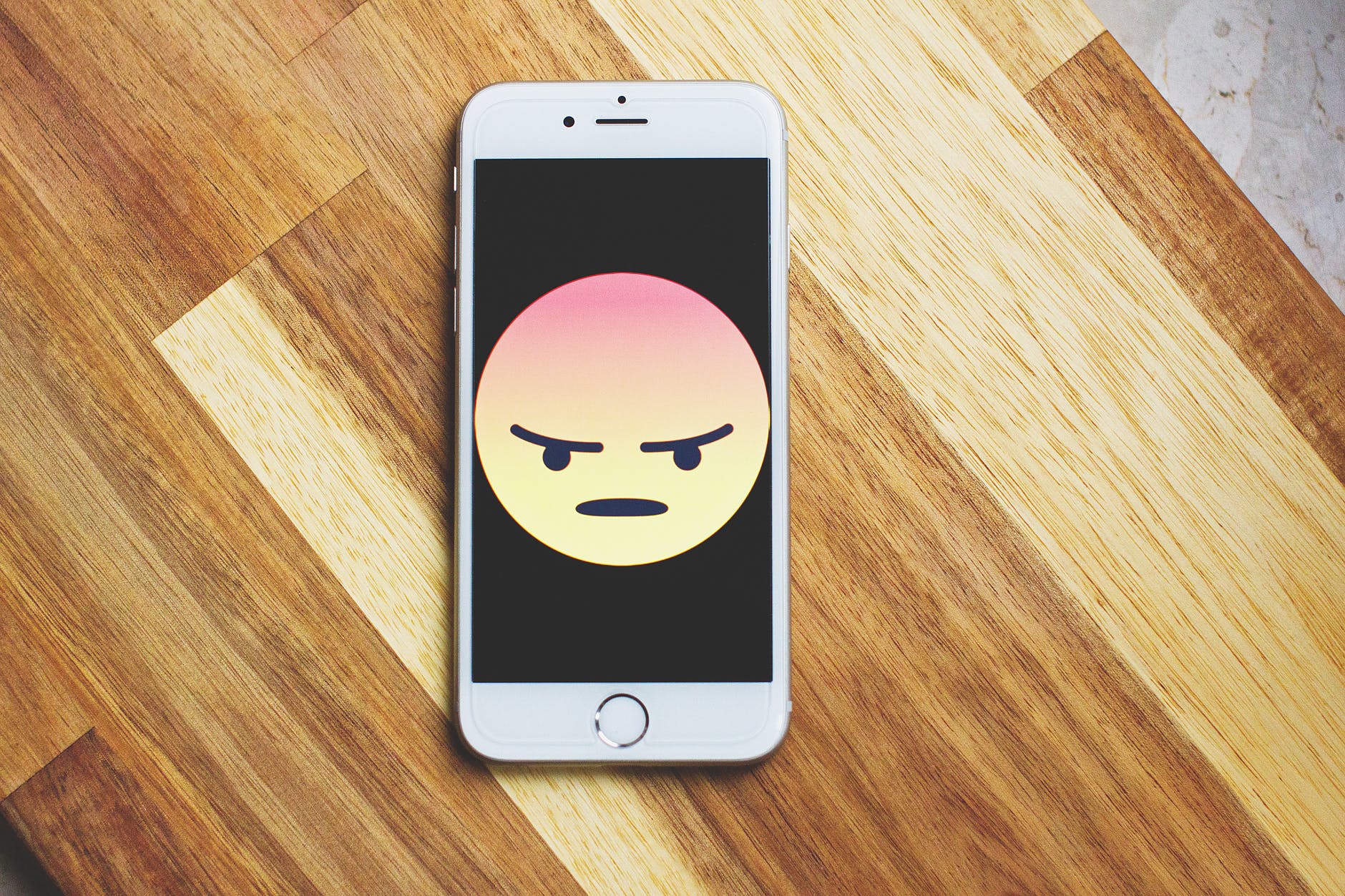 A mobile phone showing a large emoji of an angry face.