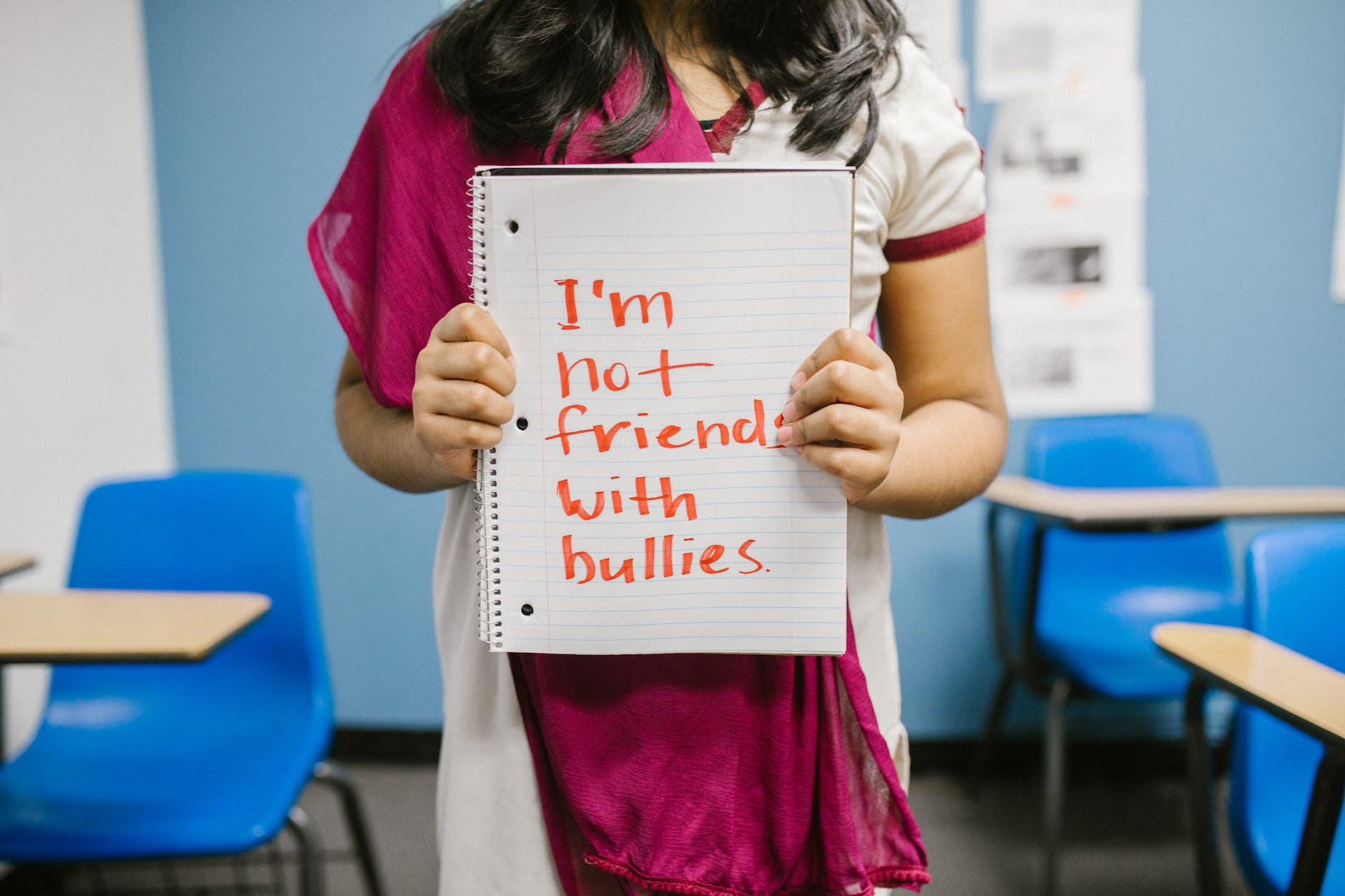 A girl in a classroom holds up the sign saying, "I'm not friends with bullies."