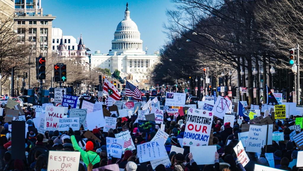 A demonstration in front of the Capital, Washington DC, with banners saying "Refugees are welcome here," and "Protecting our democracy.