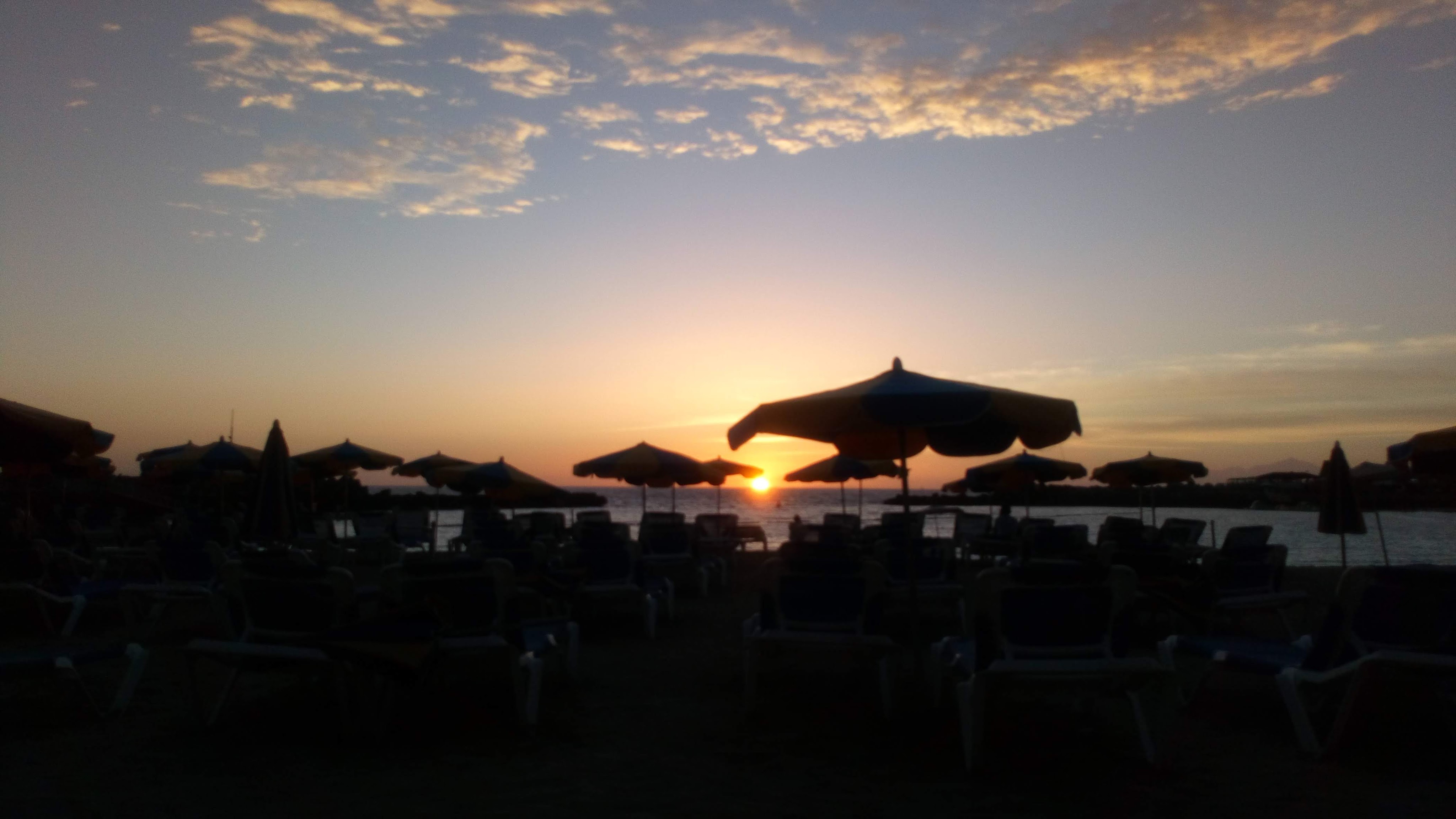 A sunset viewed through rows of sunbeds and parasols.