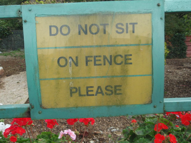 A sign fastened to a metal fence says, "Do not sit on fence please."
