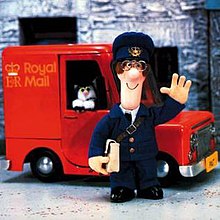 Postman Pat, a children's TV animated character stands with a parcel outside his van. In the van is Jess, his black and white cat.