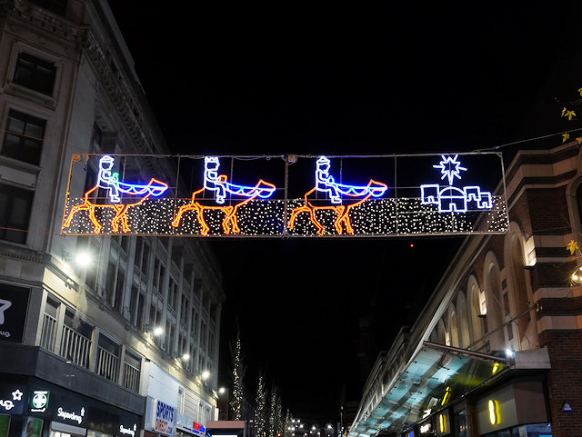 Christmas lights across a street showing three men wearing crowns riding on camels towards a small number of houses with a large star above them.