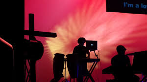 Musicians in silhouette in front of a patterned screem playing music in church.